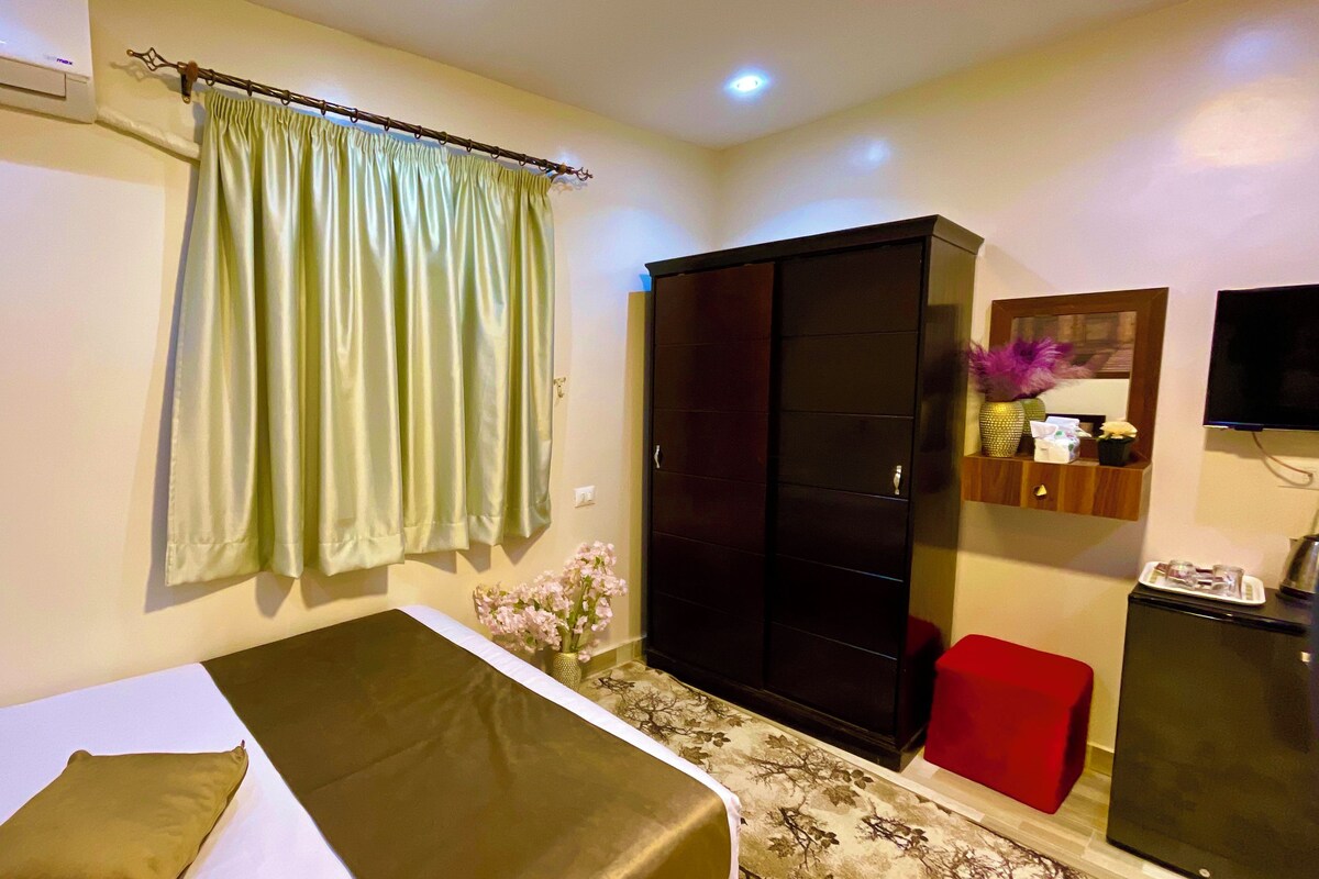 Une chambre d’hôtel avec un lit, une armoire, une petite table sur laquelle est posé un vase de fleurs et un téléviseur sur un meuble.