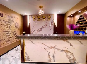 Un comptoir d’accueil surmonté d’un plateau en marbre, un mur décoratif orné d’une carte et un lustre.