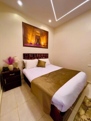 A modern hotel room with a large bed, a nightstand with a lamp, and a wall-mounted painting. - Nemes Pyramids View Inn (Giza)