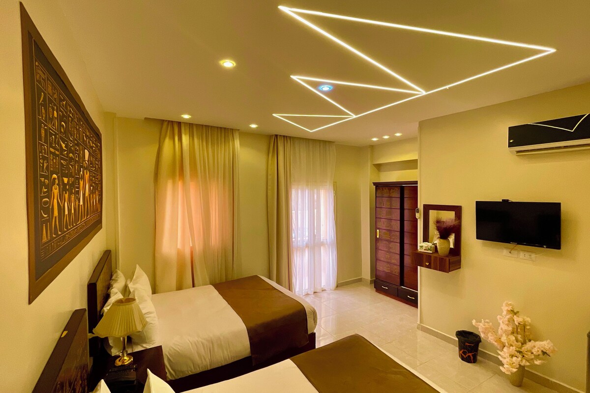 A modern hotel room with a bed, a flat-screen TV, a mirror, and a decorative wall piece.