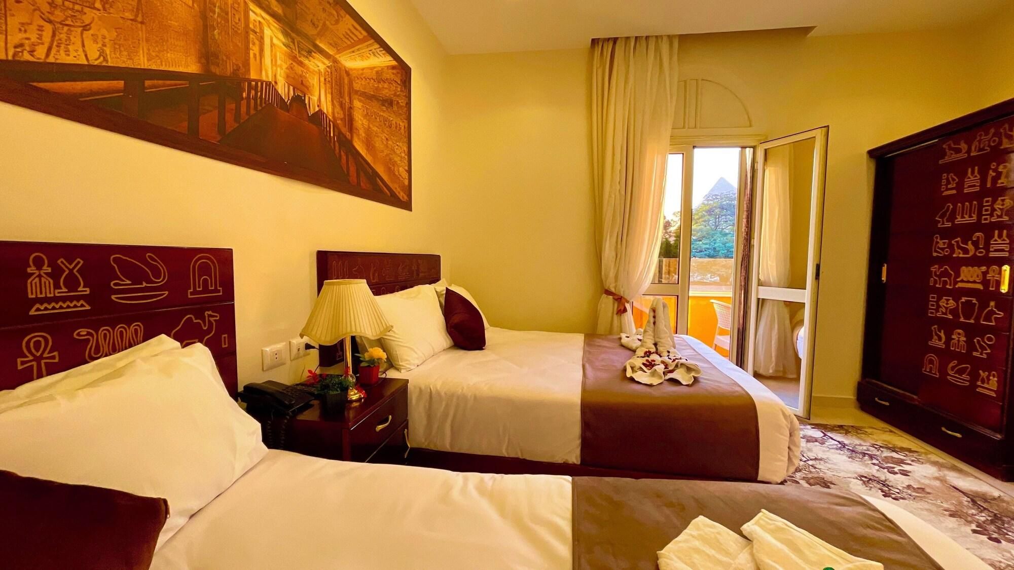 A hotel room with two beds, a nightstand, a lamp, a window with curtains, and a wall with hieroglyphs.