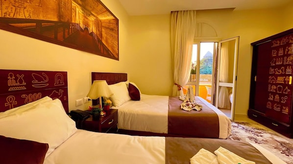 A hotel room with two beds, a nightstand, a lamp, a window with curtains, and a wall with hieroglyphs. - Nemes Pyramids View Inn (Giza)