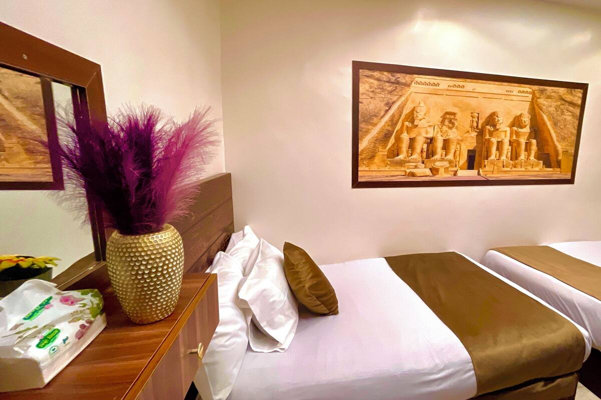 A hotel room with two beds, a wooden dresser, a mirror, and a framed picture of Egyptian figures on the wall.