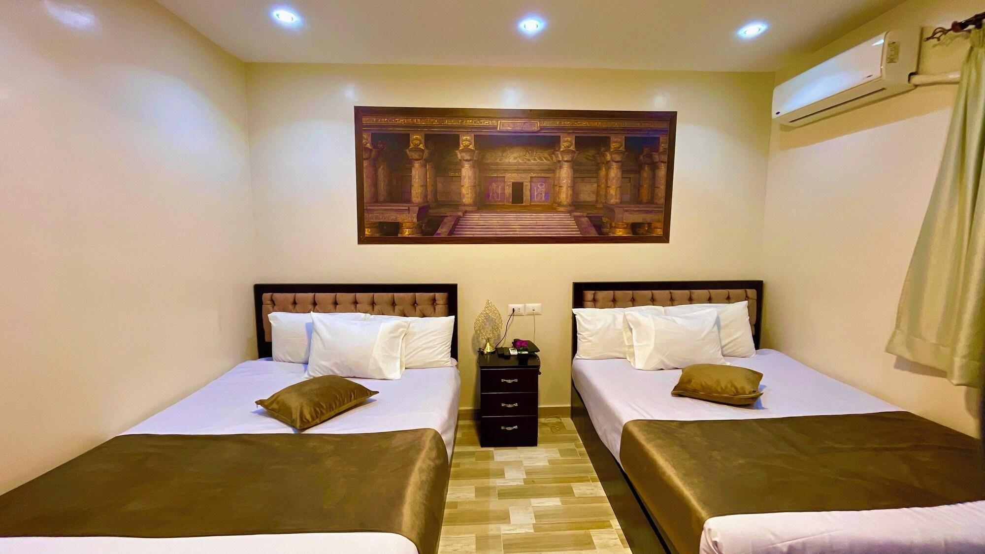 Hotelkamer met twee bedden, een nachtkastje, een wandairconditioner en een ingelijste foto boven de bedden.