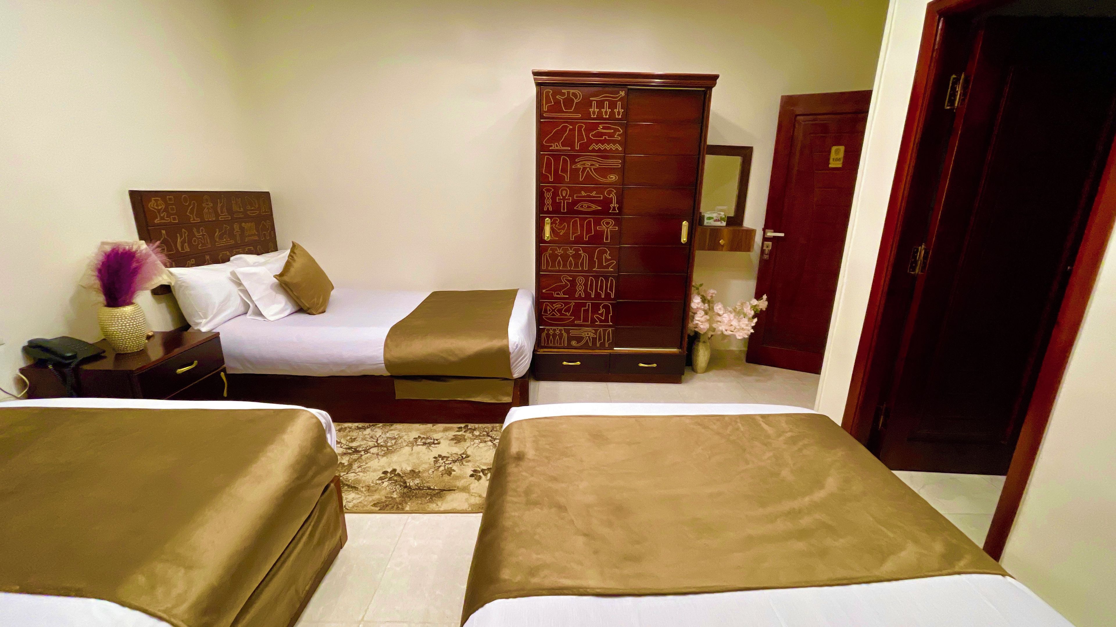 Una habitación de hotel con dos camas, un armario de madera, una mesita de noche y un espejo.