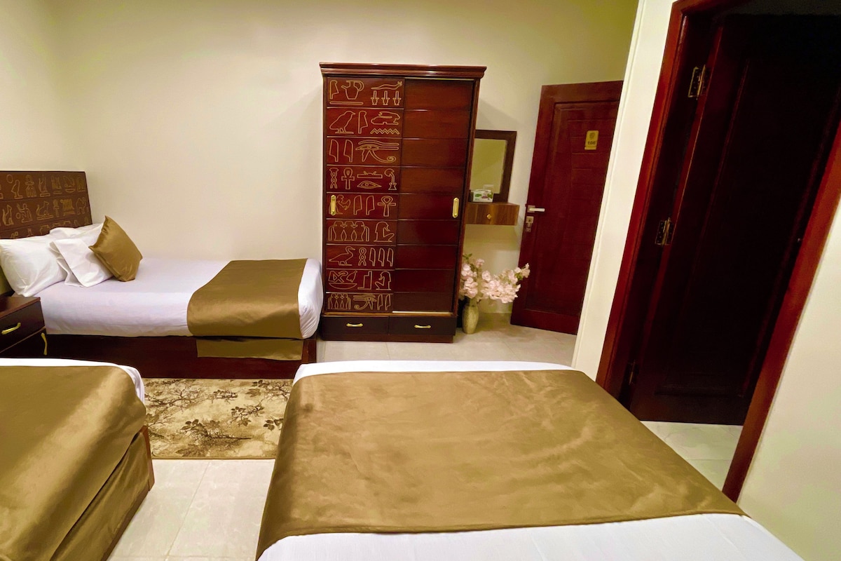 A hotel room with two beds, a wooden wardrobe, a nightstand, and a mirror.