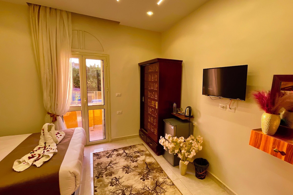 A hotel room with a bed, a desk, a television, a wardrobe, and a small table with a vase of flowers.