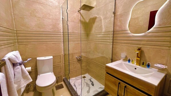 A bathroom with a toilet, shower, sink, and mirror.