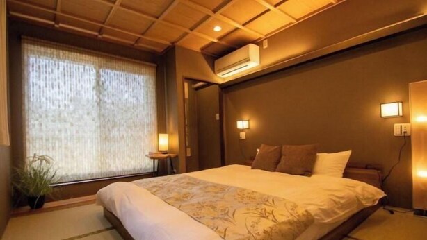 A hotel room with a large bed, a ceiling fan, an air conditioning unit, and a window with curtains. - Core Base Sumiyoshi (Fukuoka)