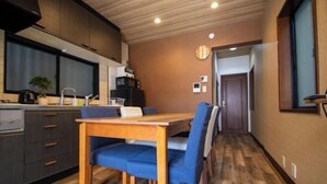 A compact kitchen with dark cabinets, a wooden dining table, and blue chairs. - Core Base Sumiyoshi (Fukuoka)