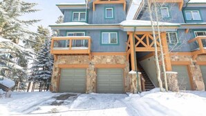 Une maison à étages avec une façade en pierre, des balcons en bois et un escalier menant au garage.
