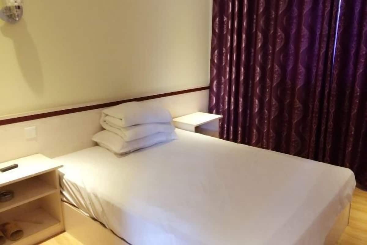 Une chambre d’hôtel avec un lit, une table de chevet, une lampe et un rideau.