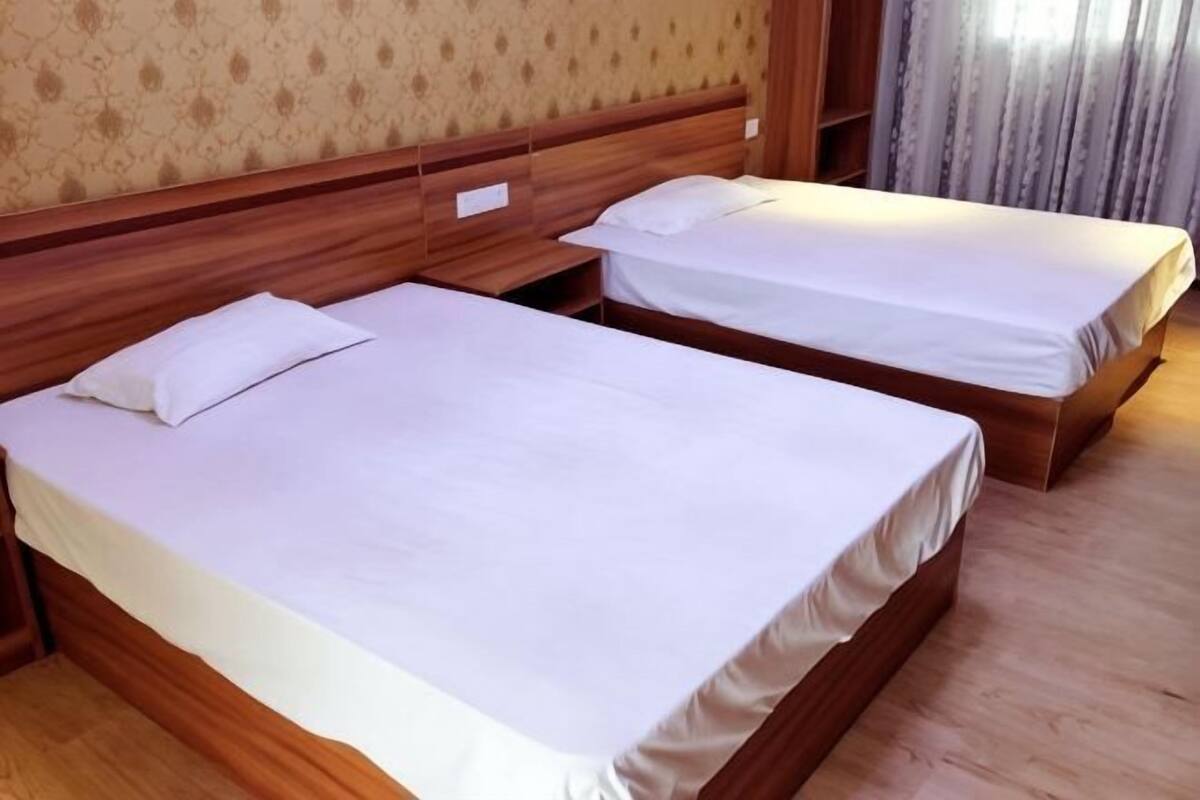 Une chambre d’hôtel avec deux lits en bois, une tête de lit en bois et un papier peint à motifs.