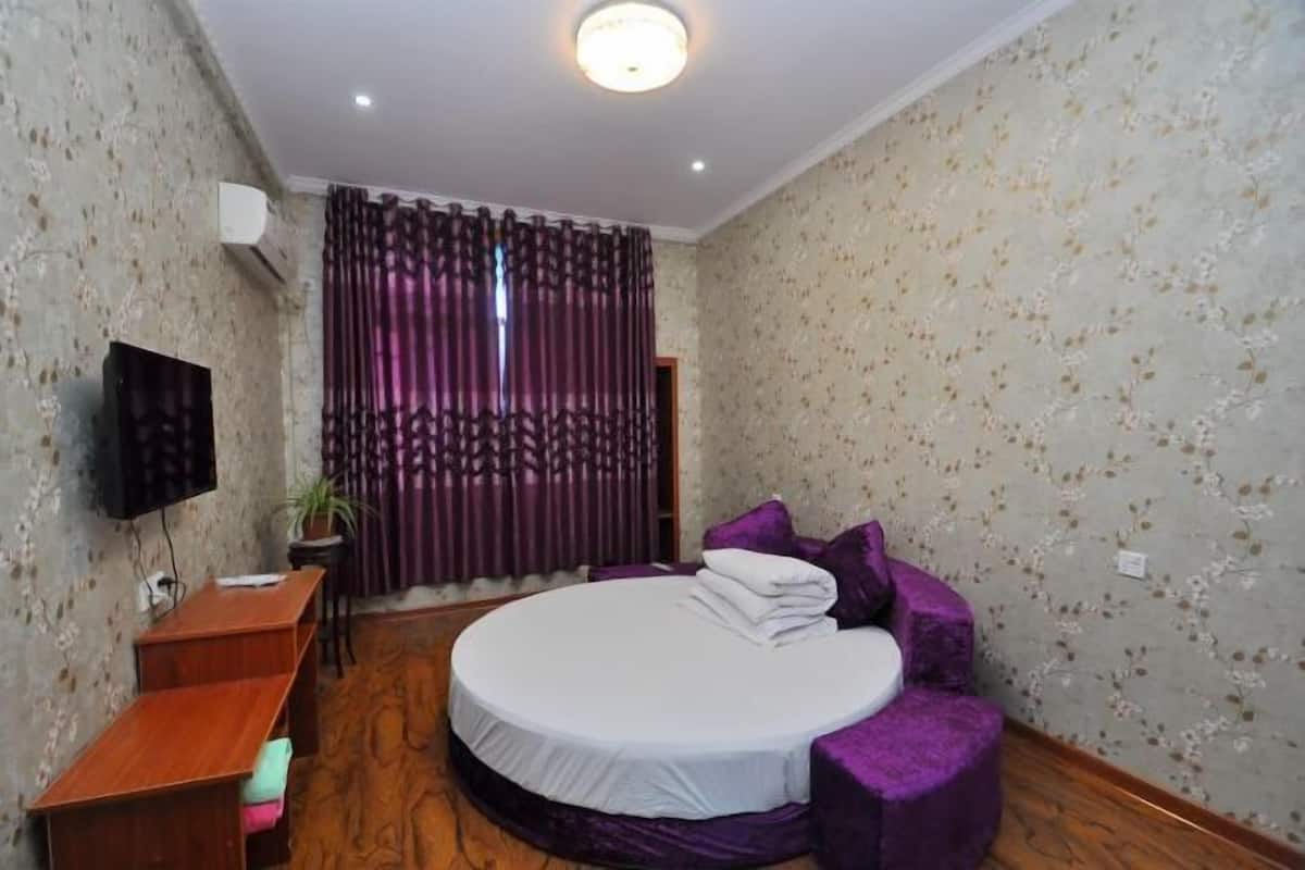 Une chambre à coucher avec un lit rond, une télévision, un bureau et une fenêtre avec des rideaux.