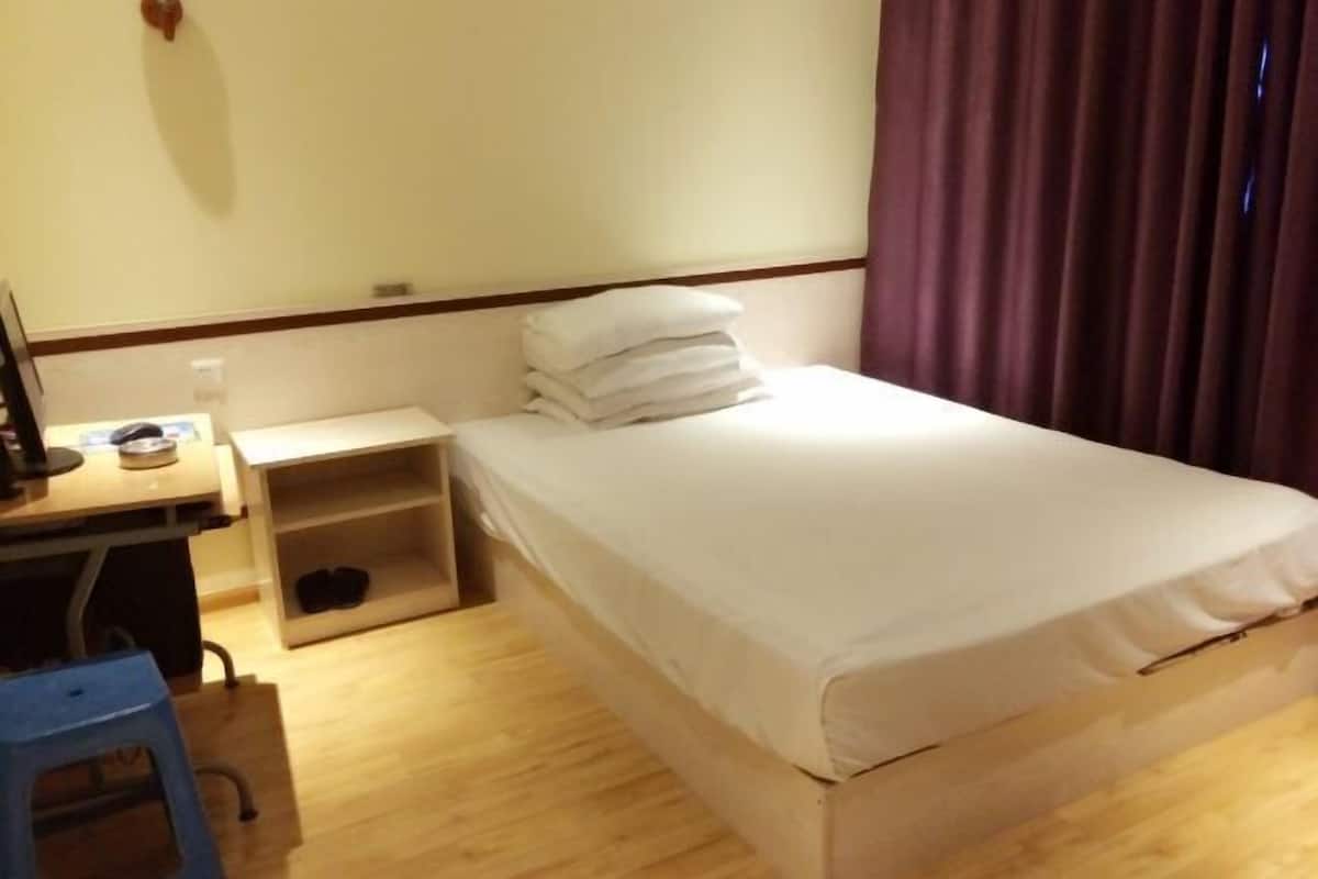 Une chambre d’hôtel avec un lit, un bureau et une chaise, une étagère avec des chaussures et une fenêtre avec des rideaux.