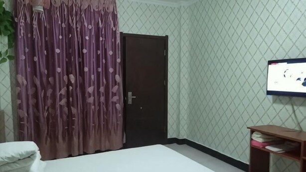 A bedroom with a bed, a wooden nightstand, a TV, and a door. - Fengyang Xiangyang Hotel (Fengyang)