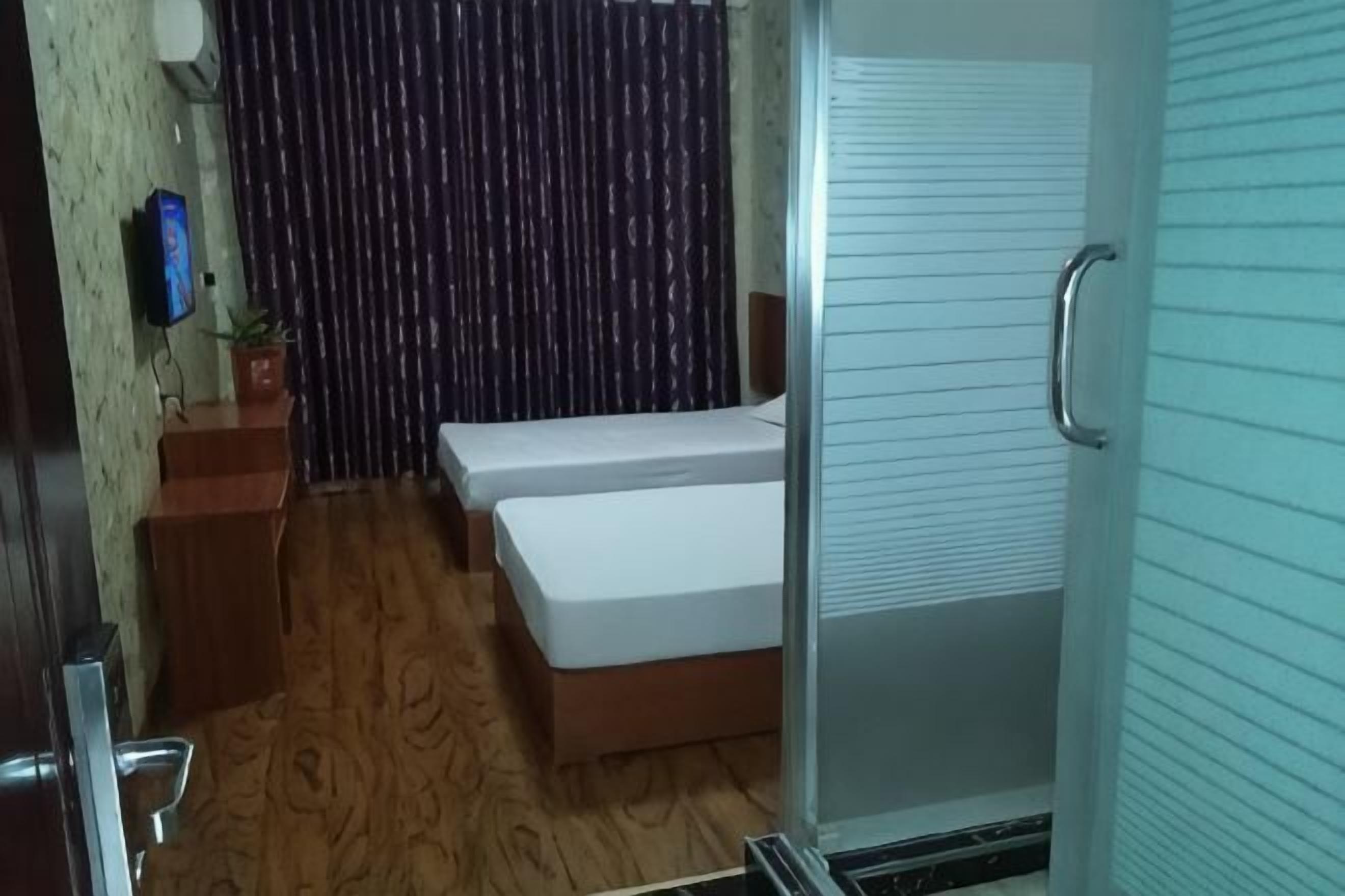A room with a bed, a small wooden table with a plant, a wall-mounted TV, and a sliding door.