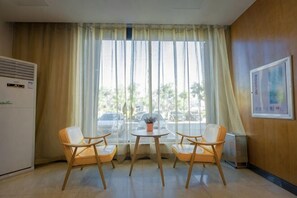 Camera d'albergo con zona pranzo, due sedie, un tavolino, una finestra con tende e un condizionatore d'aria a parete.