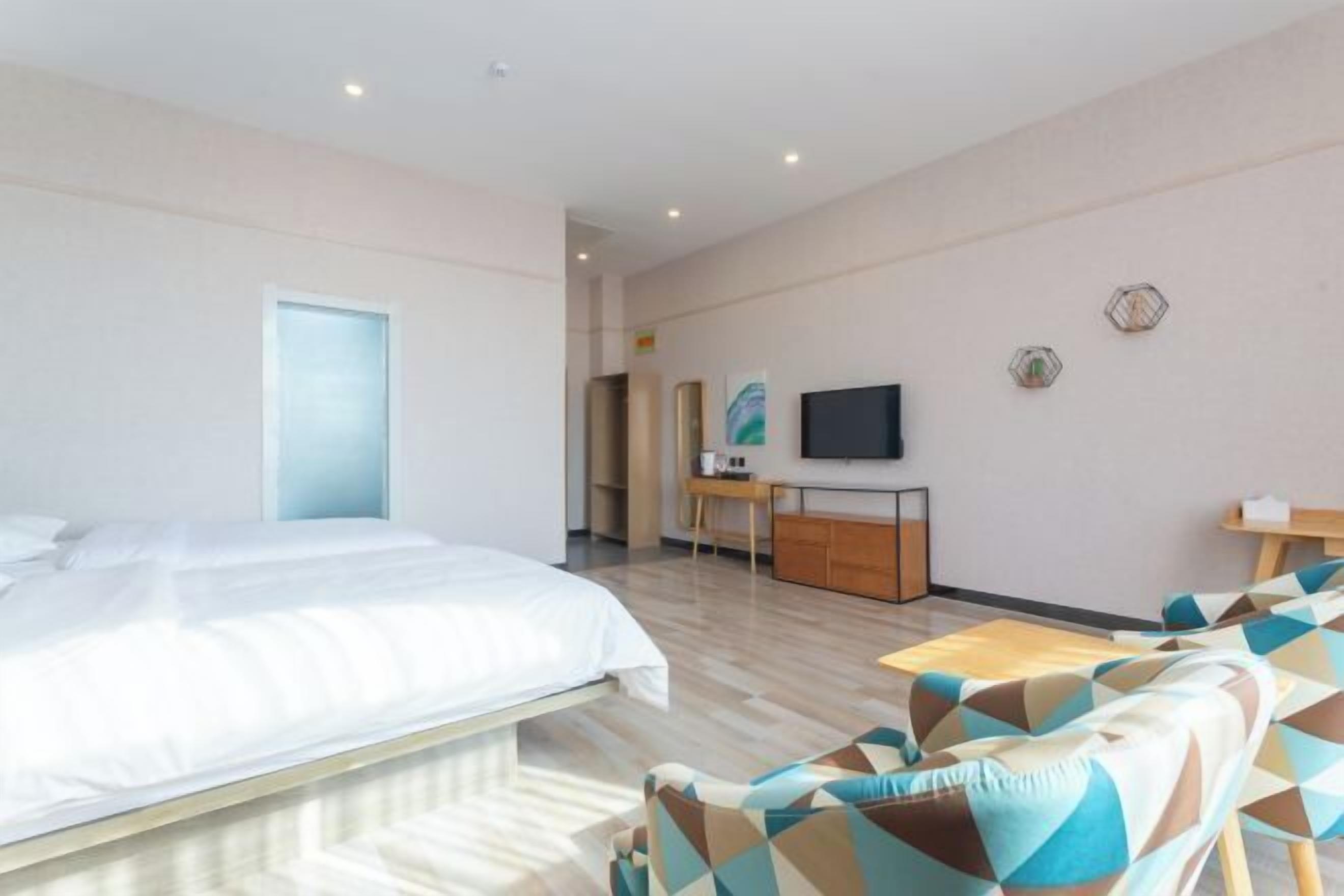 A modern hotel room with a large bed, a desk with a flat-screen TV, and a sofa with patterned cushions.
