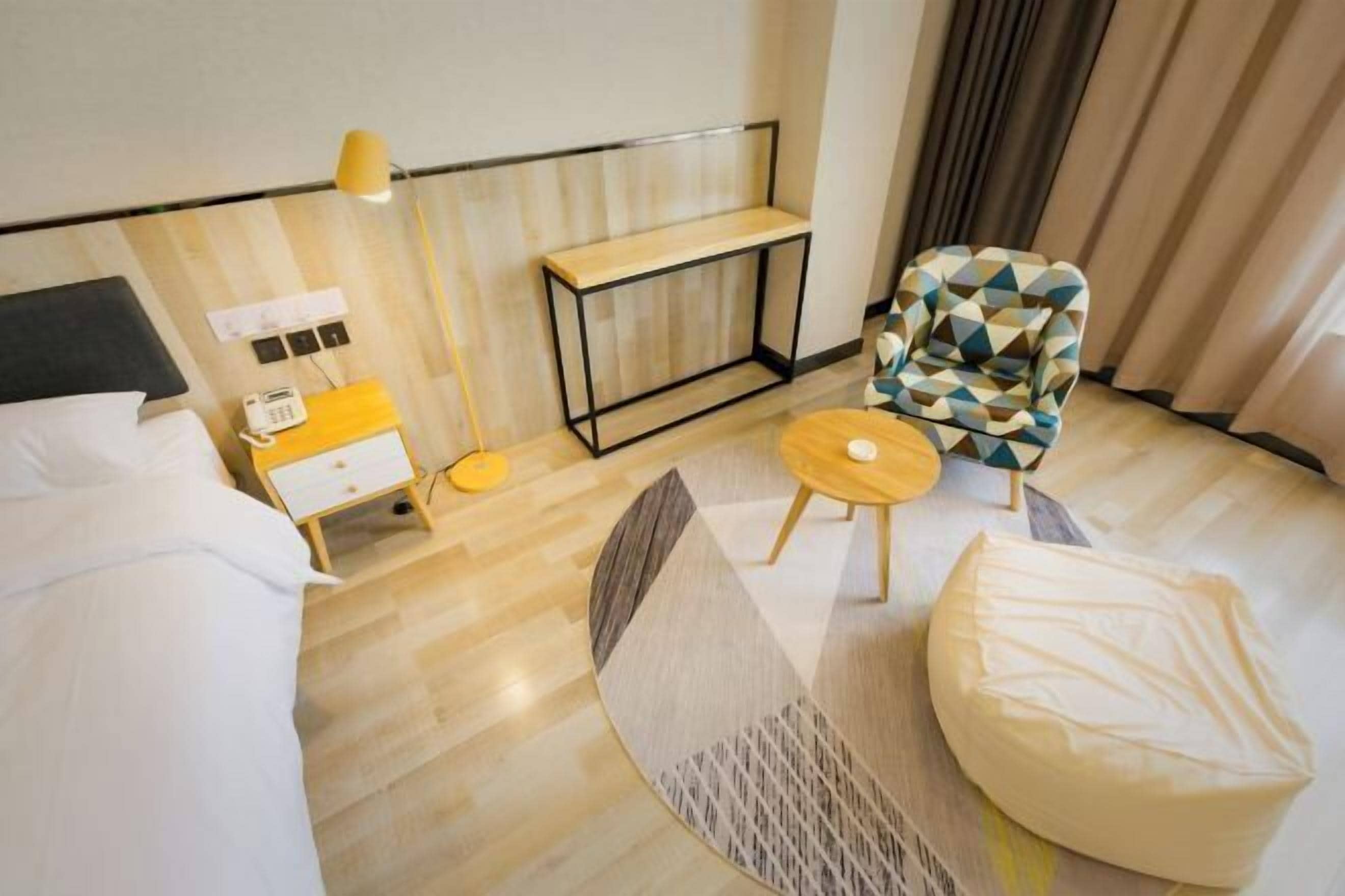 A hotel room with a bed, bedside table, lamp, chair, and a small round table.