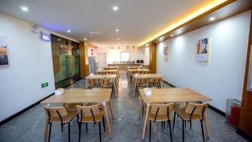 Un comedor de hotel con varias mesas y sillas, una cocina al fondo y un diseño moderno y limpio.