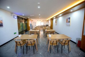 A hotel dining area with multiple tables and chairs, a kitchen in the background, and a clean, modern design. - Shankee Tea Style Hotel (Qingdao Jiaodong International Airport Haier Avenue) (Jiaozhou)