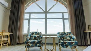 A room with a large arched window, two patterned armchairs, a small table, and a wooden chair. - Shankee Tea Style Hotel (Qingdao Jiaodong International Airport Haier Avenue) (Jiaozhou)