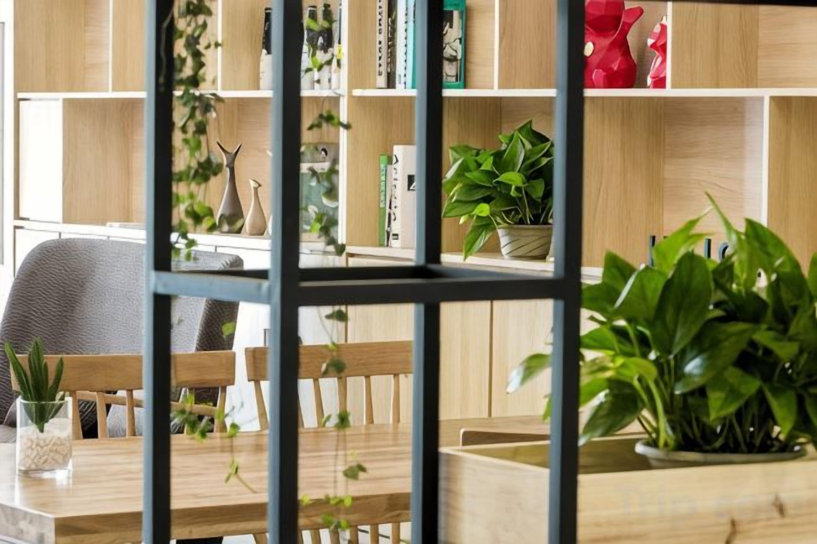 Une pièce comprenant une table à manger en bois, des chaises, une bibliothèque remplie de livres et d’objets décoratifs, ainsi que des plantes en pot.