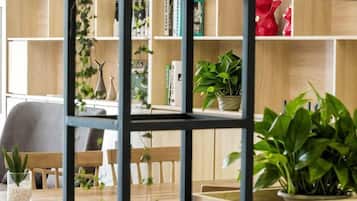 Une pièce comprenant une table à manger en bois, des chaises, une bibliothèque remplie de livres et d’objets décoratifs, ainsi que des plantes en pot.