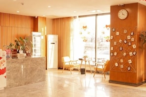 A hotel reception area with a marble counter, wooden paneling, a clock, and a wall decorated with small pictures. - Shankee Tea Style Hotel (Qingdao Jiaodong International Airport Haier Avenue) (Jiaozhou)