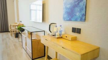 A hotel room with a wooden desk, a flat-screen TV, a coffee maker, and a painting on the wall.