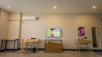A hotel room with a flat-screen TV, a wooden desk, a chair, a small cabinet, and a mirror on the wall.