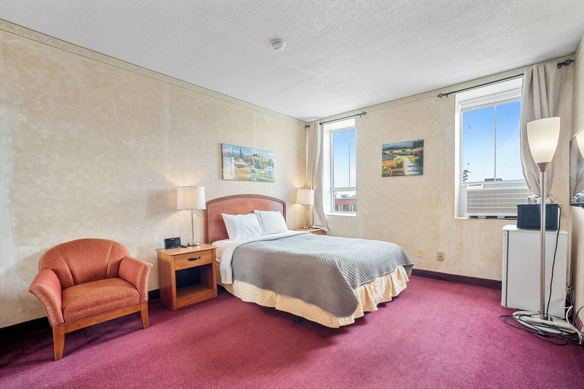 A hotel room with a bed, a chair, a desk, and a lamp.