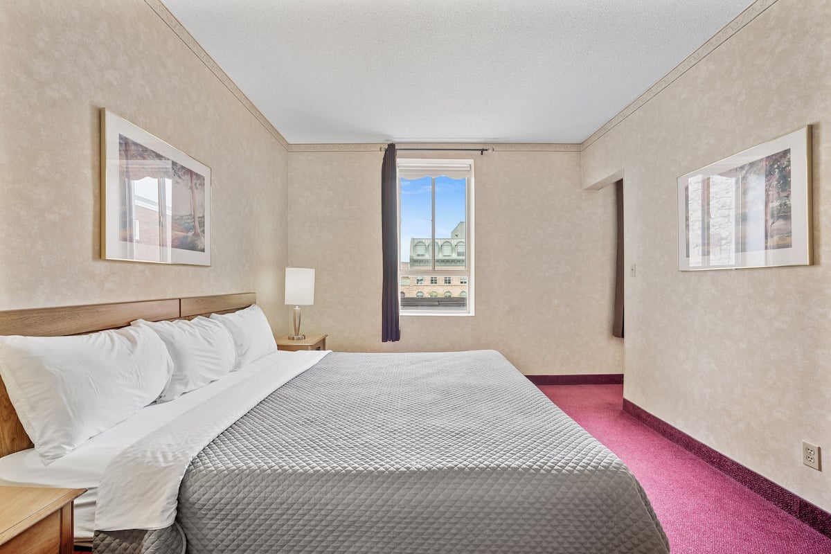 A hotel room with a bed, a nightstand, a window with a curtain, and two framed pictures on the walls.