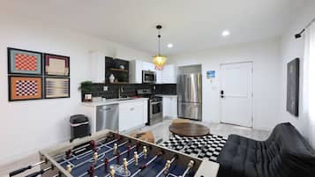 Cozinha moderna com mesa de futebol de bolso, sala de jantar com mesa xadrez e sofá preto.
