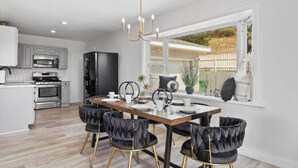 Cozinha moderna com área de jantar, com um lustre, uma janela ampla com vista e uma mesa de jantar posta para quatro pessoas.