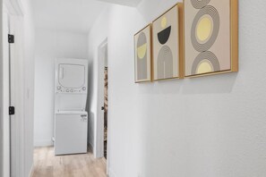 A hallway with a white wall, a door, and a refrigerator. There are three framed artworks on the wall.