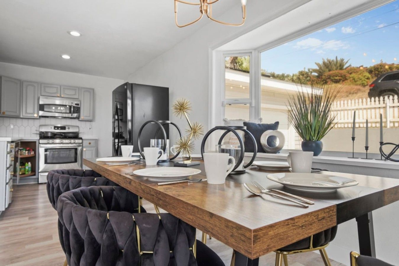 A modern kitchen with a wooden dining table, black chairs, and a view of the outdoors.