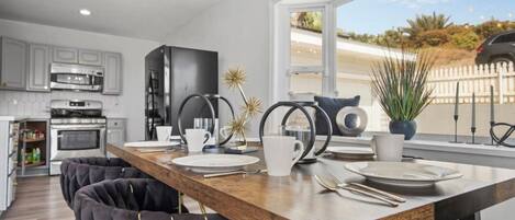 A modern kitchen with a wooden dining table, black chairs, and a view of the outdoors.