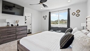 A bedroom with a bed, a dresser, a ceiling fan, a window with curtains, and wall decorations. - 5bed/3ba, Gameroom, Pool, Spa, Sleeps 20+, Views (San Diego)