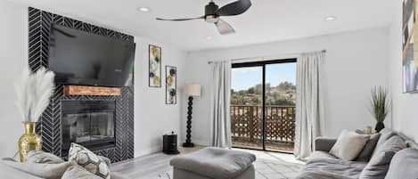 Una sala moderna con chimenea, ventilador de techo y balcón con vistas.