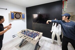 A room with a foosball table, dartboard, and a television on the wall.