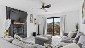 A modern living room with a fireplace, a ceiling fan, and a large window with a view of the outdoors. - 5bed/3ba, Gameroom, Pool, Spa, Sleeps 20+, Views (San Diego)