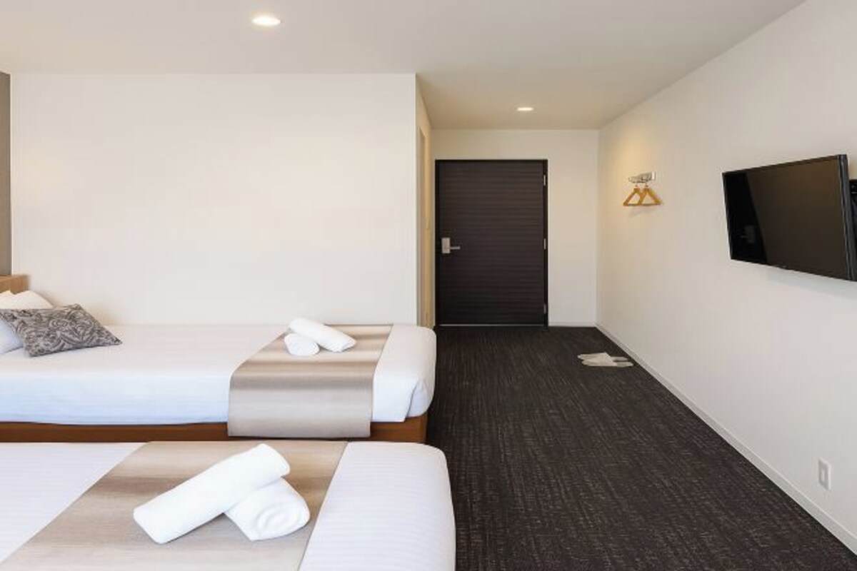 A hotel room with two beds, a flat-screen TV, a door, and a wall-mounted light fixture.