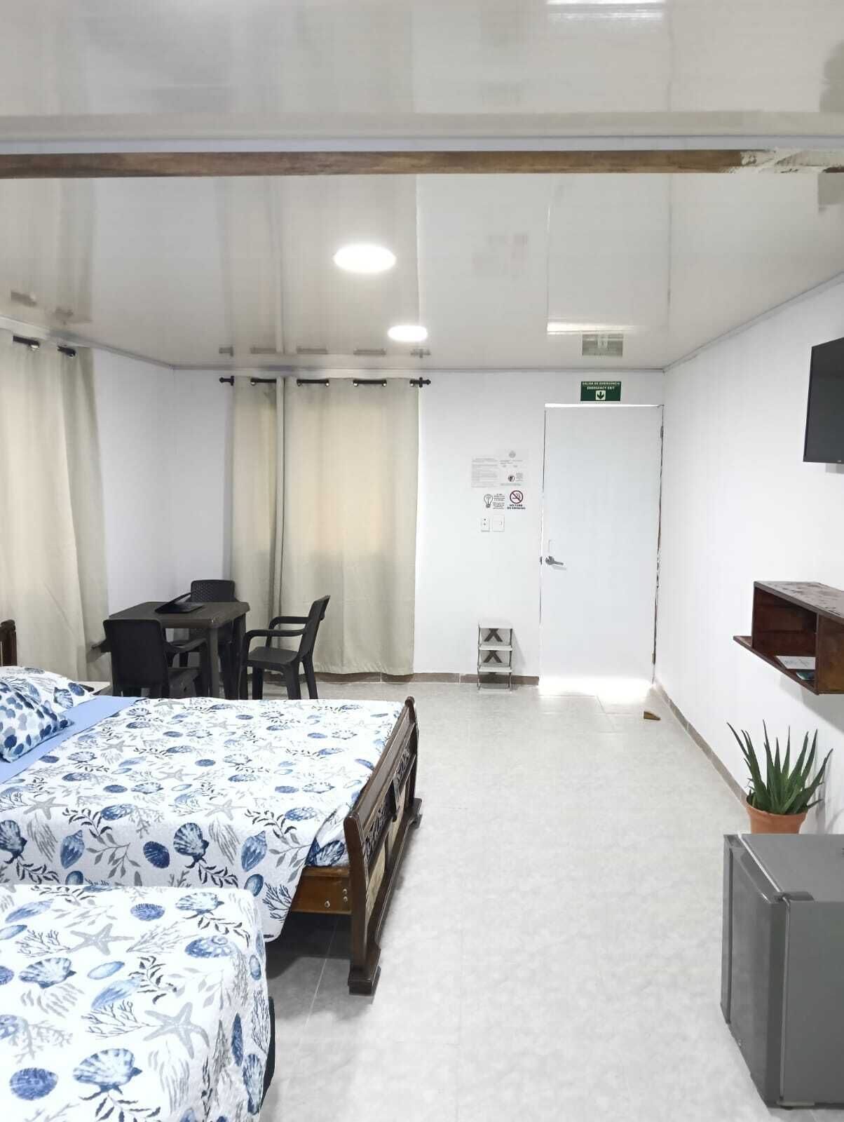 A hotel room with a bed, a desk, chairs, a television, and a potted plant.