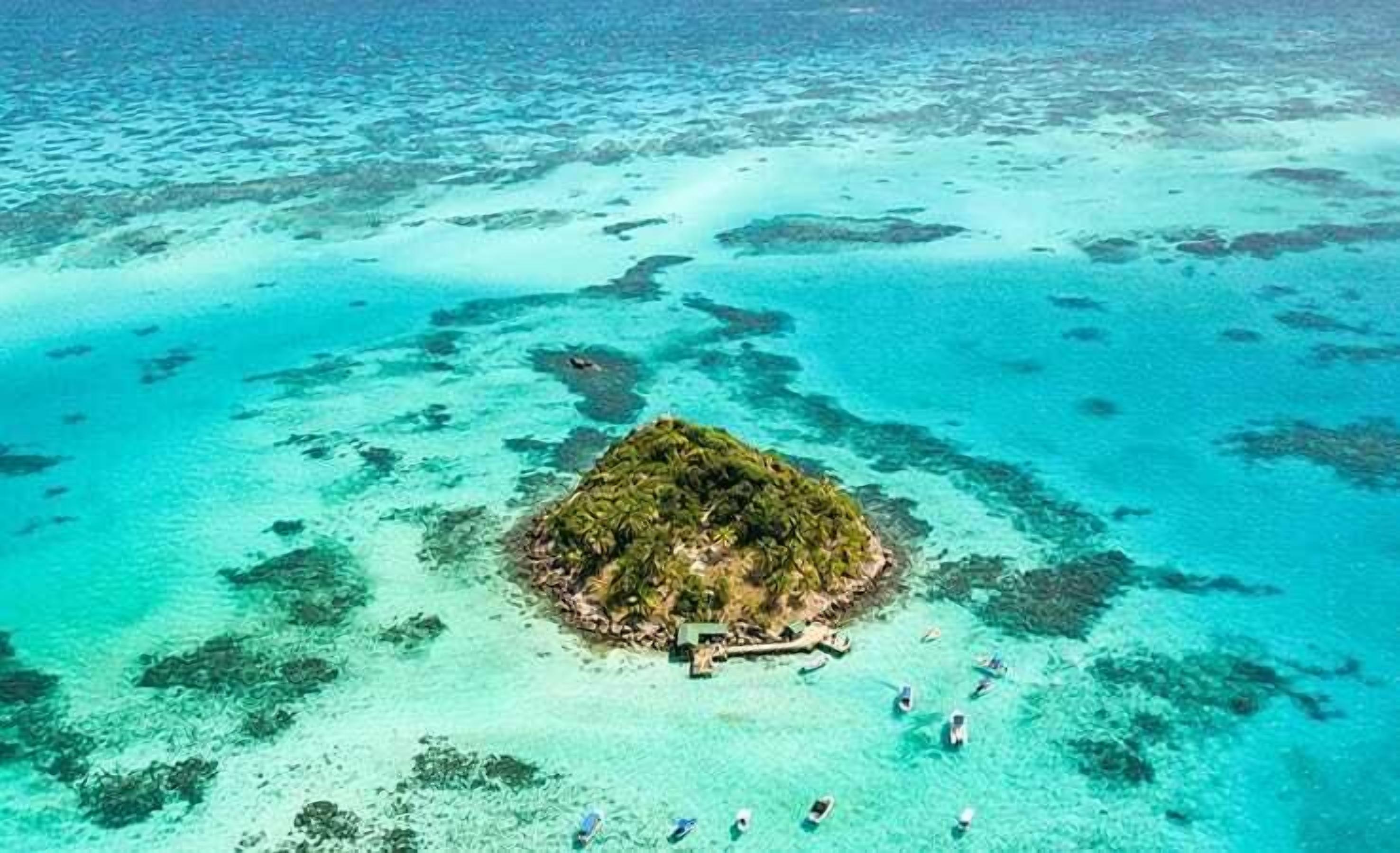 An aerial view of a small island with clear turquoise waters and a few boats.