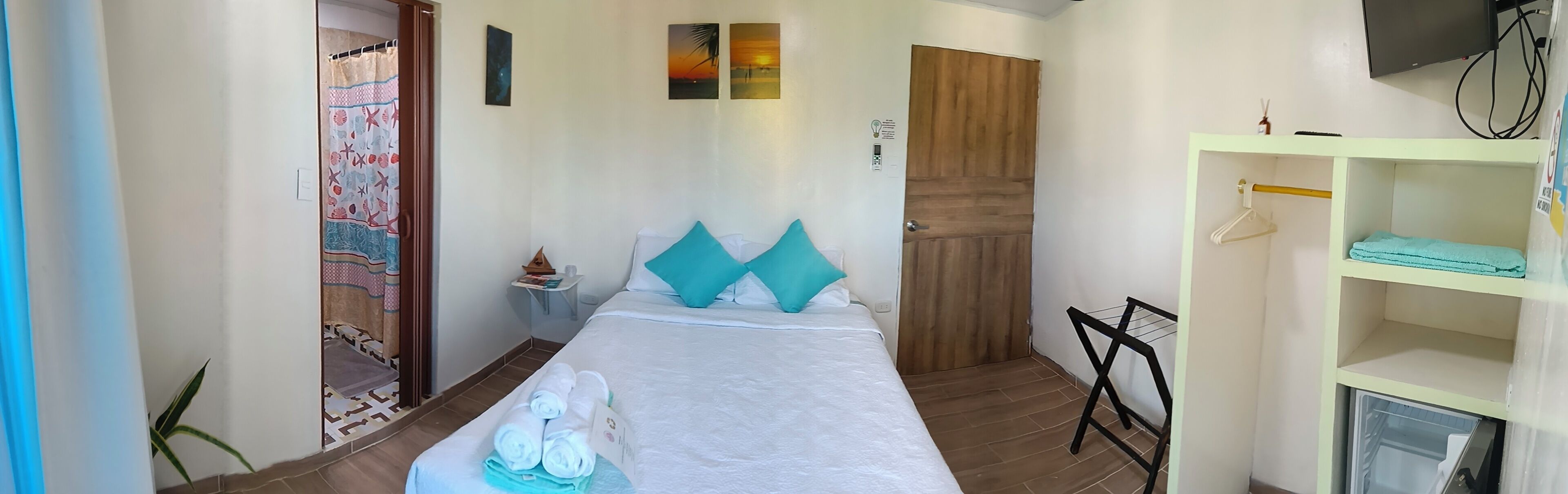 Une chambre d’hôtel avec un lit, une porte en bois, une étagère avec des cintres et un téléviseur fixé au mur.