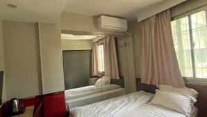 Ein Hotelzimmer mit zwei Betten, einem Schreibtisch, einer Klimaanlage und einem Fenster mit Vorhängen.