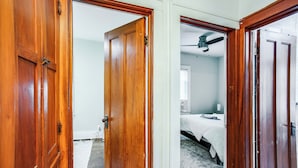 A room with a wooden door, a bed with a white bedspread, and a ceiling fan.