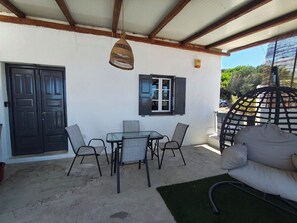 A covered outdoor seating area with a table and chairs, a hanging light fixture, and a door.